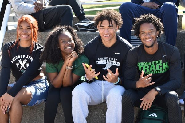 Four Chicago State University track and field athletes smiling while sitting together on bleachers.&nbsp;
