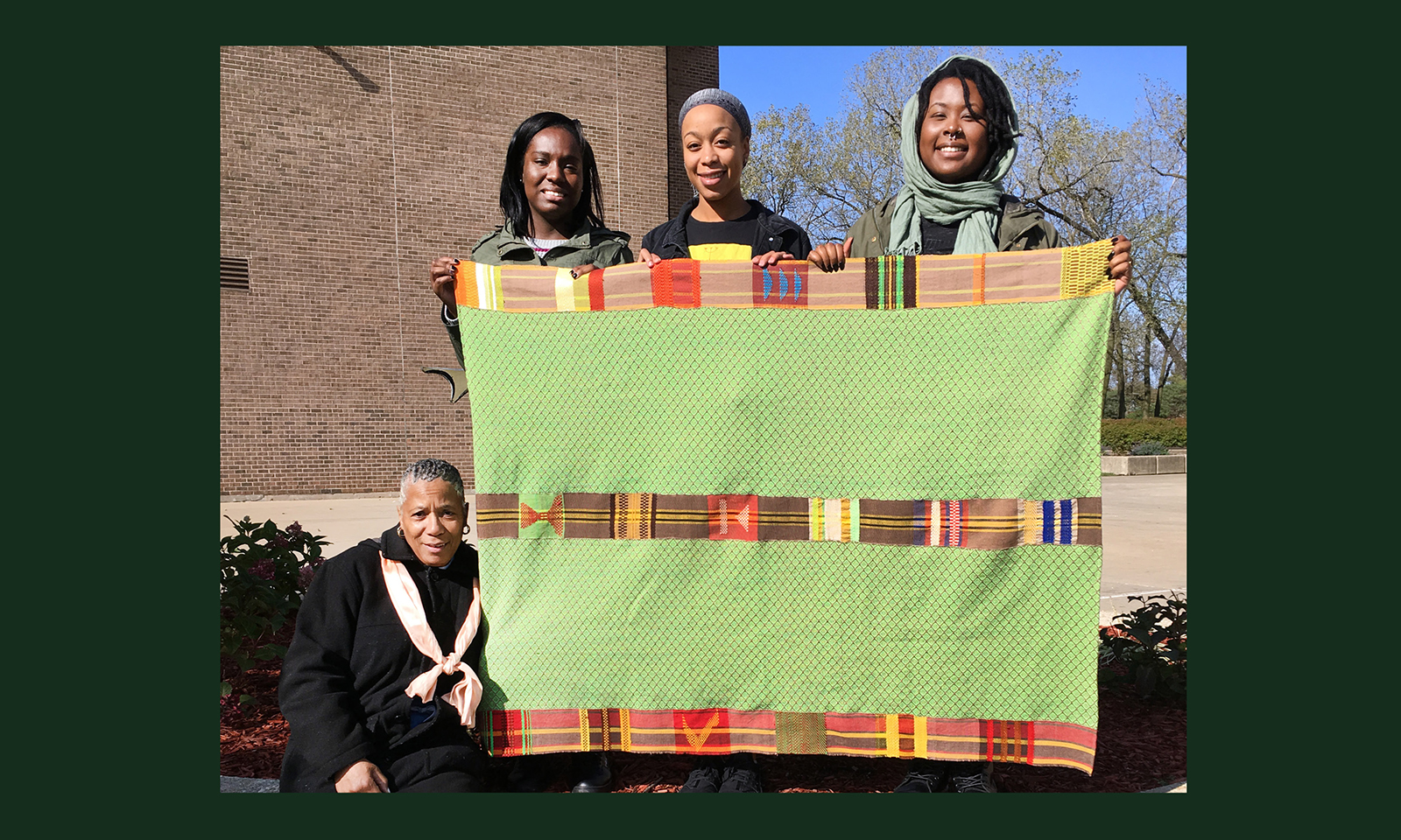 Four students holding textile art quilt