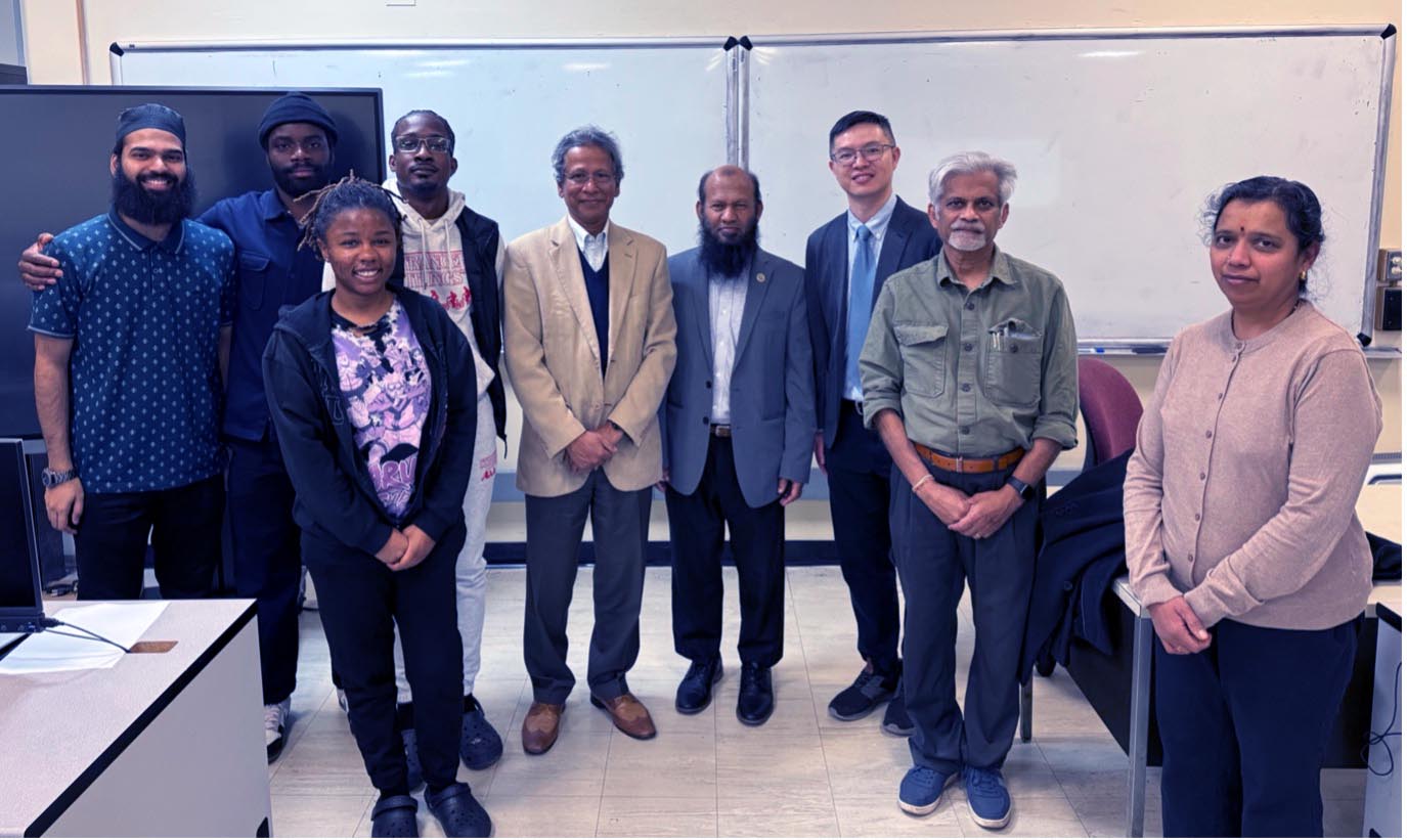 A group of students and faculty members smile and stand next to each other in front of a large white board.