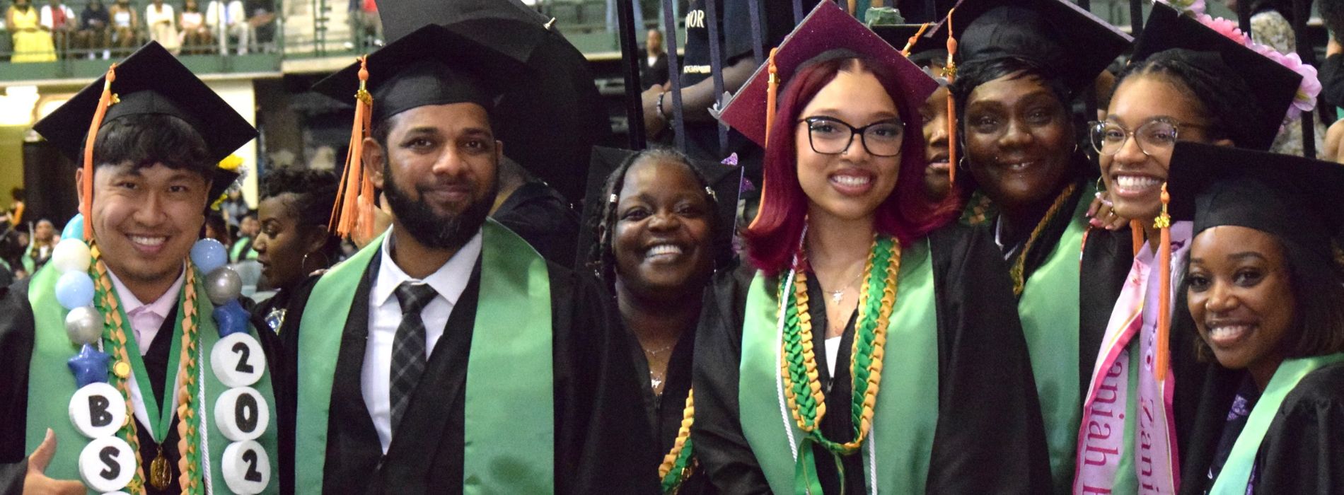 Seven Chicago State University graduates posing together and smiling in black graduation caps and green stoles during the commencement ceremony.