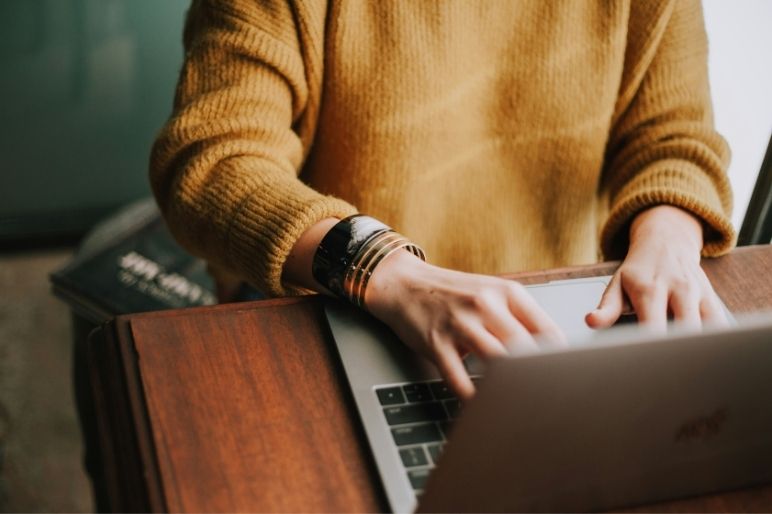 A person is seen typing on a laptop, their hands resting on a wooden desk.