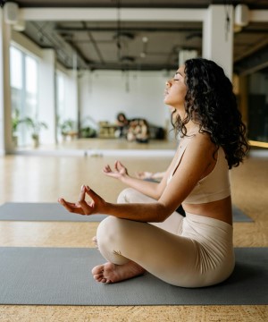 A woman sits on a yoga mat with her eyes closed in a meditation pose