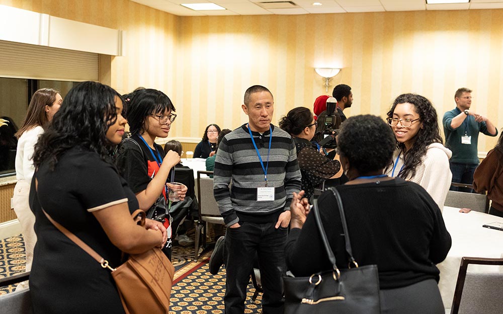 Five people in a brightly lit conference room stand closely together in a circle, engaged in conversation.