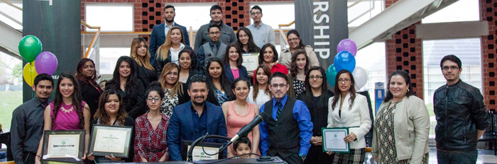 A group photo of about thirty people smiling on the stairs of the rotunda in the student union building. A few of them in the front are holding certificates. There are brick columns and multi-colored balloons behind them.