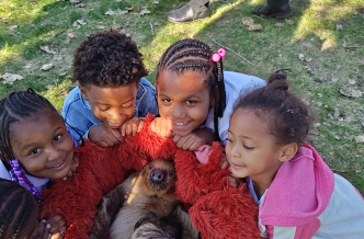 Four children in a semicircle holding a baby sloth