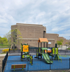 photo of the playground with the College of Education in the background. The playground features slides and climbing structures on a blue cushioned surface