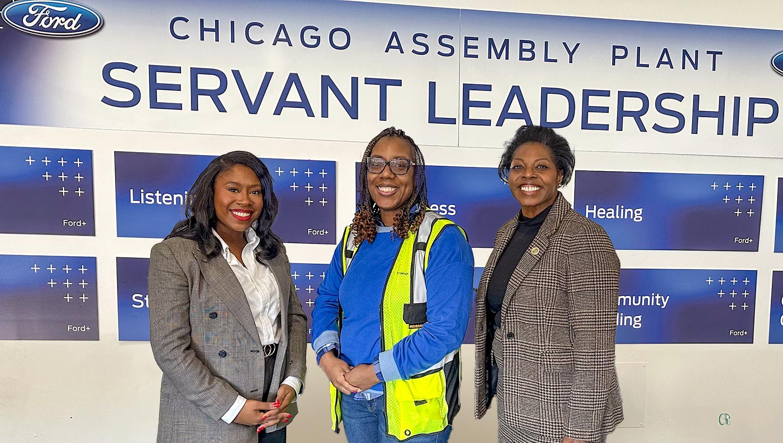 Three women standing in front of a Ford Chicago Assembly Plant sign detailing "Servant Leadership" principles.